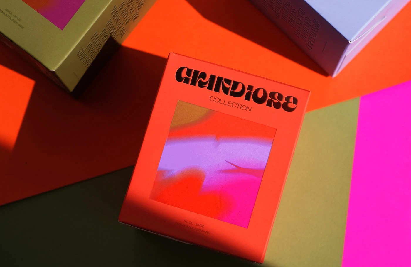 glassware brand identity — amber and violet ribbed tall glasses on yellow and lavender surface, Grandiose Collection by Agostina Benaglia